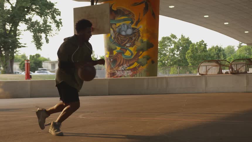 Young black man playing basketball on outdoor court under overpass