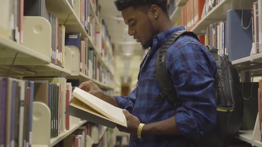 A man stands in a library aisle reading a book