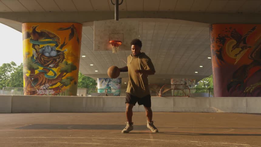 Sweaty black man plays basketball alone under the bridge at sunset