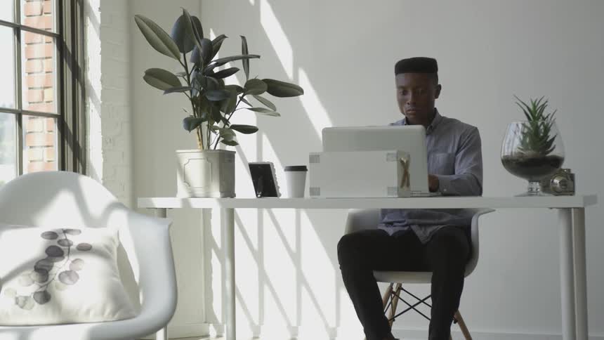 A man works on his computer while drinking coffee at a desk