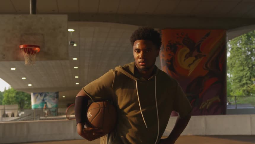Sweaty black man plays basketball under the bridge at sunset