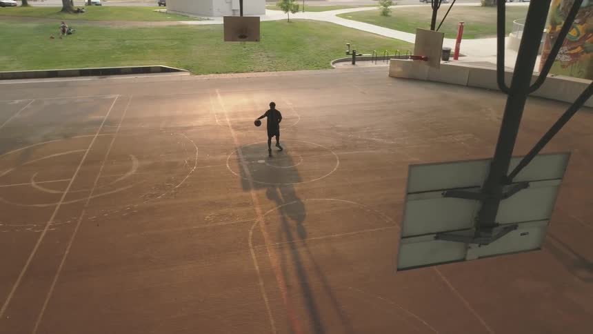 A basketball player dribbling a basketball on a basketball court under a bridge