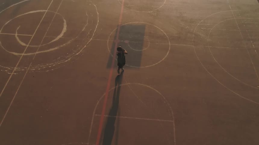 A person shooting a basketball at a hoop on a street court during the evening