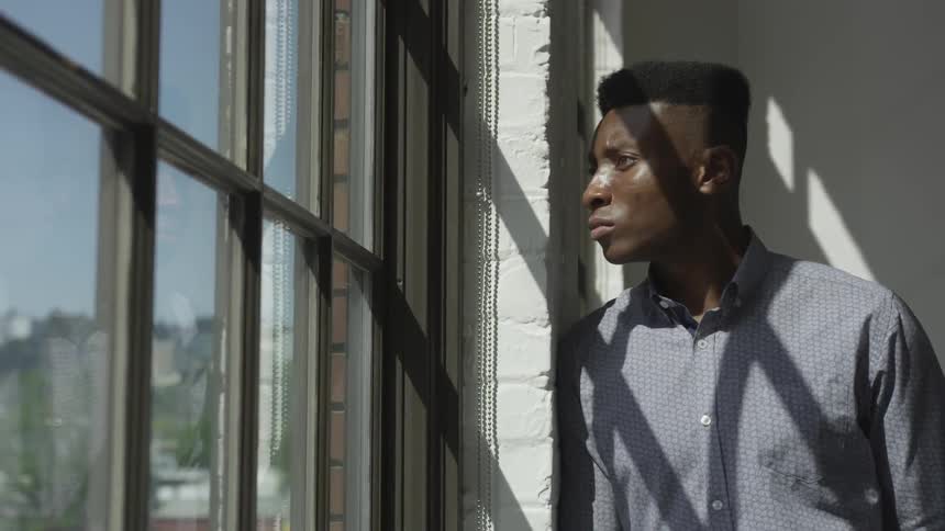 A man stands next to and looks out a window
