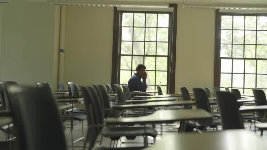 Man sits near window in empty classroom working on laptop