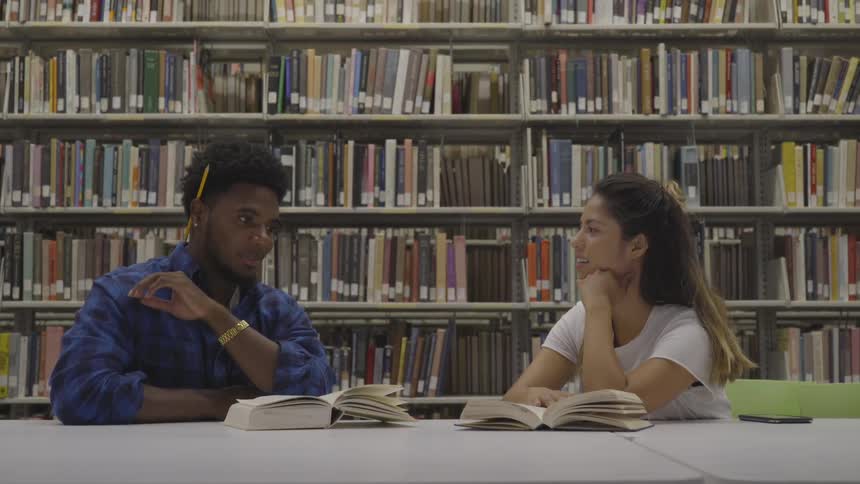 Two people talk while sitting in a library