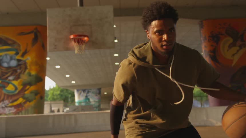 Sweaty black man plays basketball under the bridge at sunset