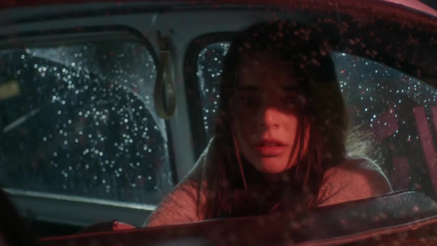 A young woman turns in concern inside a vehicle on a rainy night