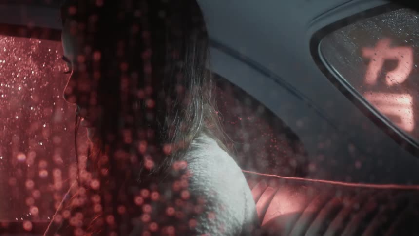 A woman sits in the backseat of a car at night in the rain