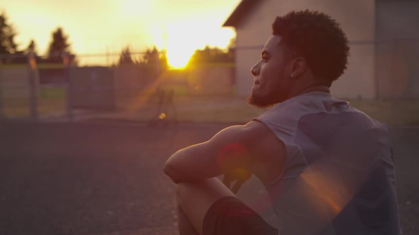 A black man sits outdoors looking into the distance