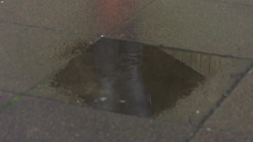 Reflection of a man in a sidewalk puddle as he roller blades through it