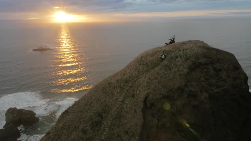 Sun setting over the ocean as a surfer climbs a steep hill to enjoy the view and contemplate life