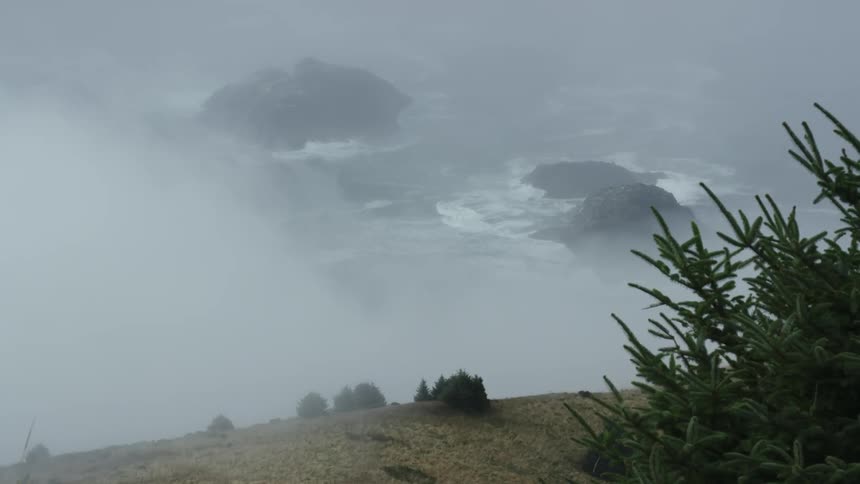 A hilltop overlooks waves crashing against large rocks in the ocean