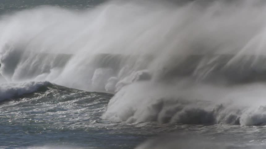 Offshore winds as a large wave foams and crashes into a massive explosion