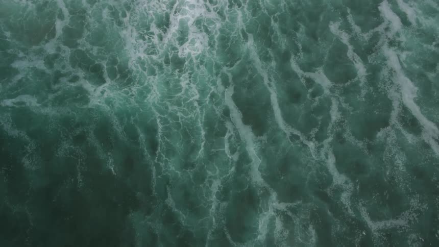 Aerial shot of the tide rushing up on shore revealing the huge ocean