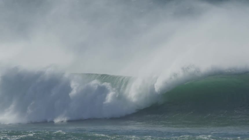 A perfectly shaped large wave rolls and crashes as offshore winds blow massive plumes of mist into the air