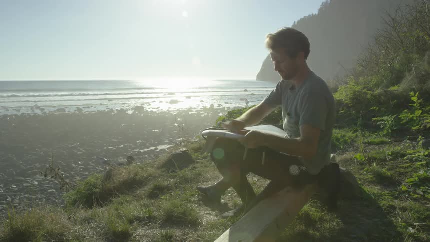 A man waxes his surfboard on the shoreline