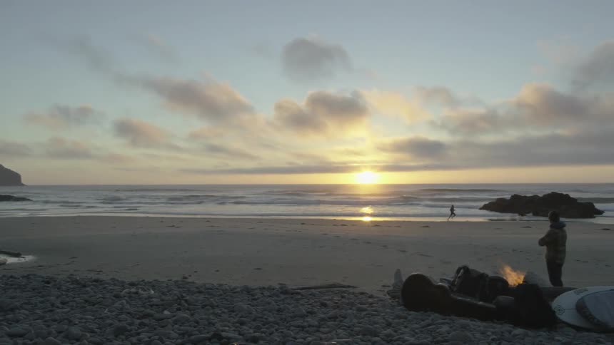 A man chases his dog on the beach at sunset