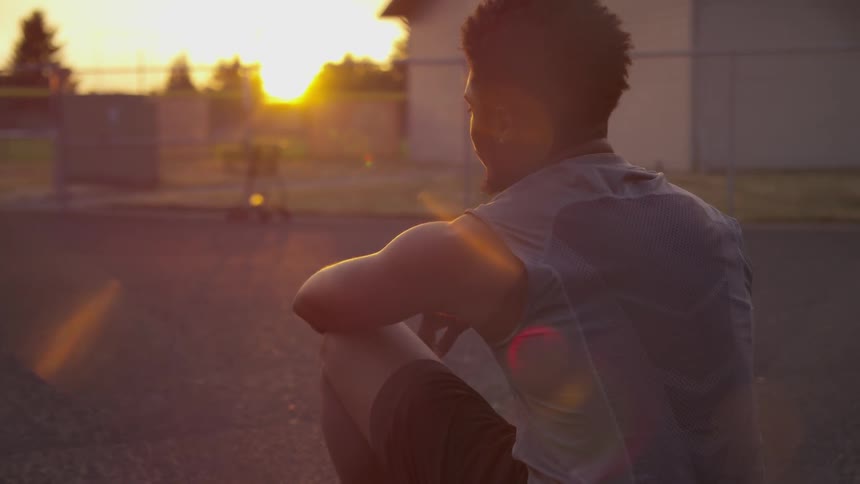 A young black man sits outside looking into the sun and then turns his head sideways