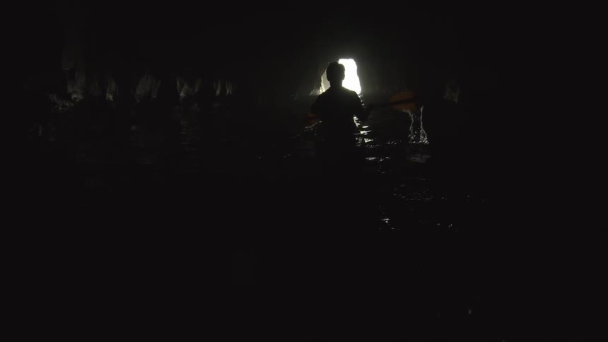 A man kayaks through a dark sea cave