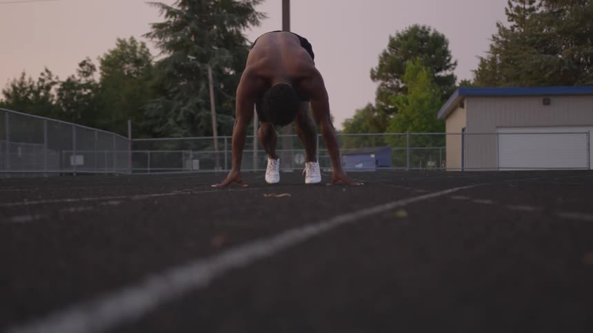 A shirtless man runs on an outdoor track at sunset