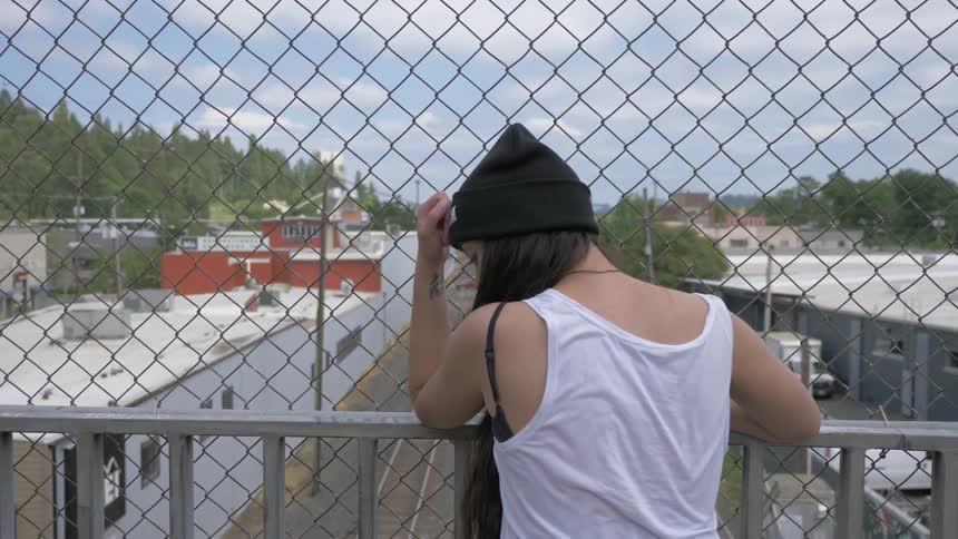 A woman stands on a bridge with a fence in front of her