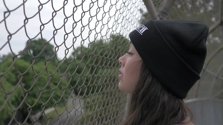 Girl teenager looks down on street from foot bridge with chain link fence surrounding it