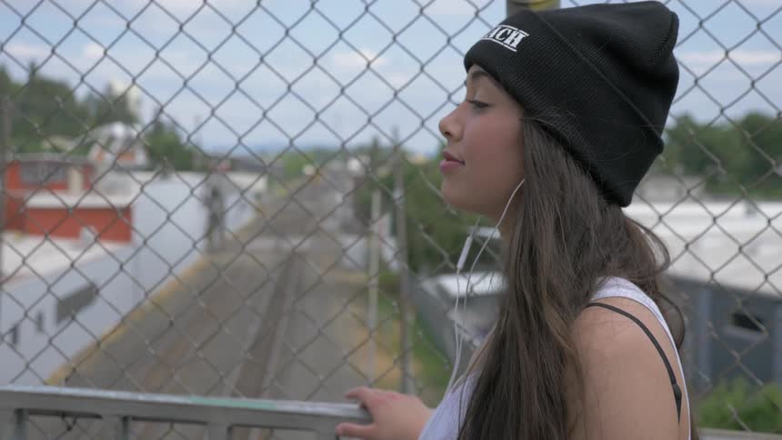 Asian woman wearing wooly hat walks on the overpass and touches banister in the daytime