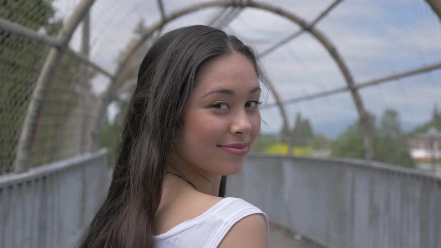 A young woman standing on a path swings her hair one way around her head and then the other
