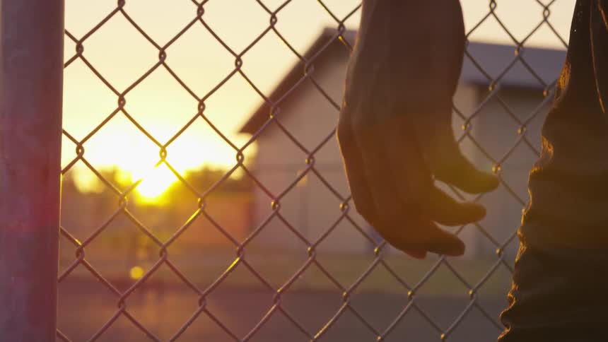Man stands near chain link fence at sunrise