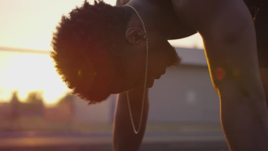 Half naked black man wearing chain necklace waits at starting position then runs at sunset