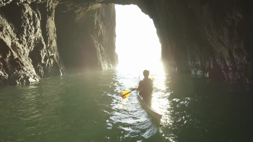 Man paddling a kayak through a rocky cave revealing an incredible sunset