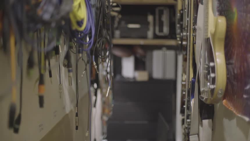 Guitars and cords hang on both sides of the walls in a narrow passage ending in shelving
