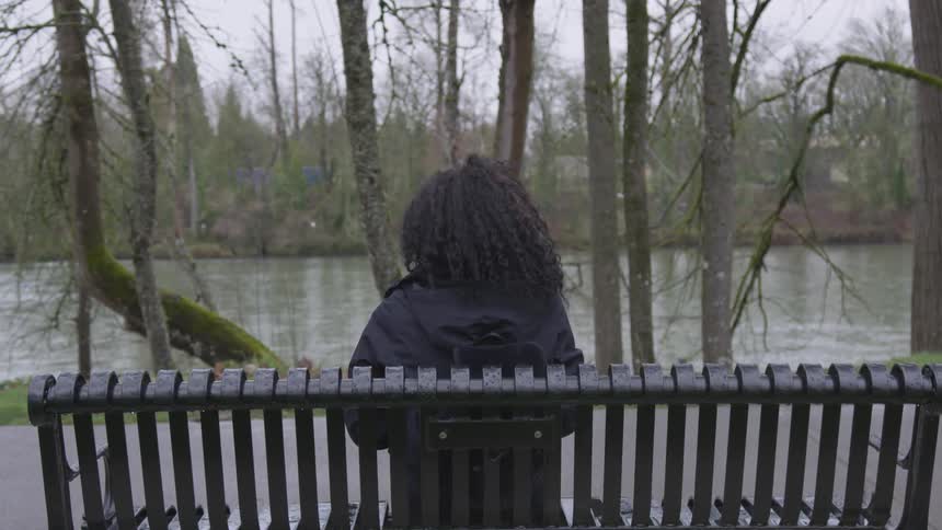 Curly hair girl sits on the bench in front of a river during daytime