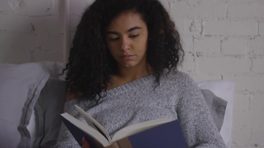 A young woman sits on a bed reading