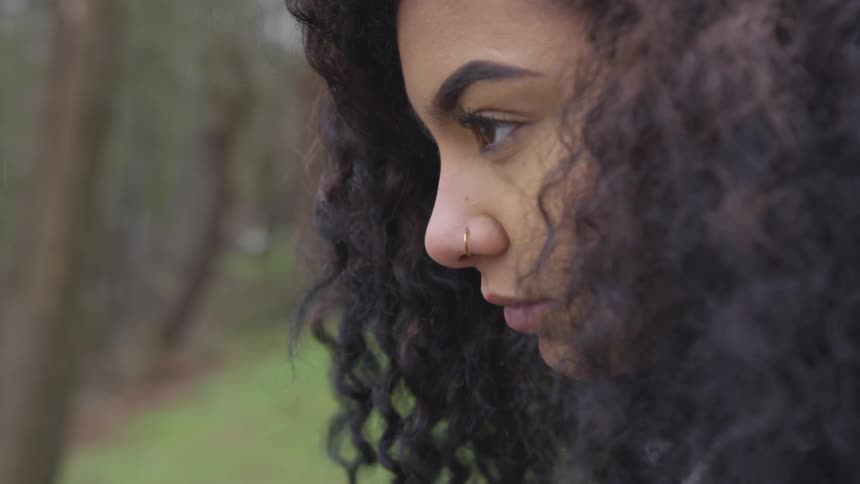 Woman with curly hair and wearing a nose ring blinks her eyes and looks up