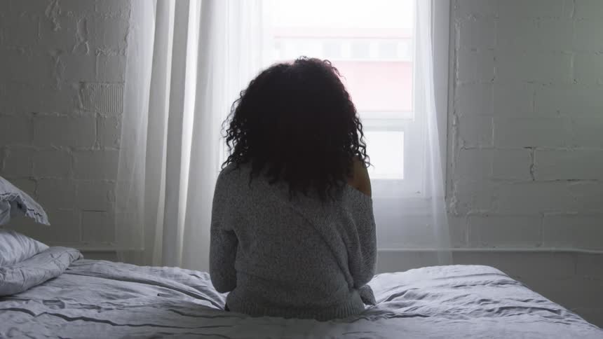 A woman sits on a bed looking out the window