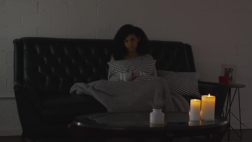 Female sitting on a leather couch covered with a blanket and candles burning nearby