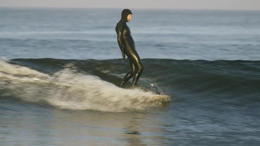 A man dressed in a black wetsuit surfs on a small wave at a beach