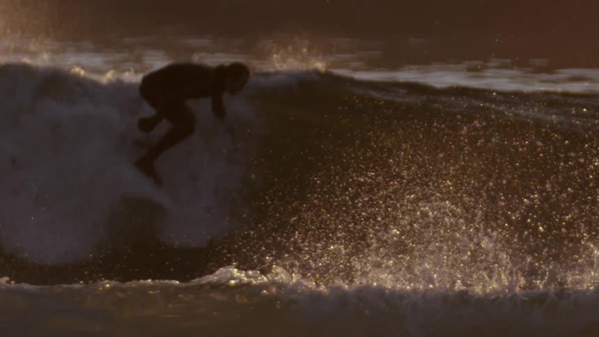 Telephoto shot of a surfer riding wave as the sun glistens and reflects off the water