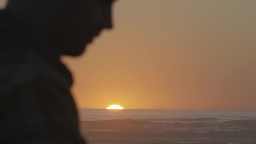 A man stands against a sunset backdrop