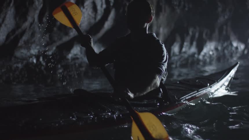 A man paddles in the water through a dark and magical sea cave