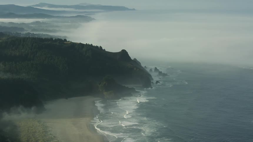 Waves crash against a hilly shoreline on the coast of a vast ocean