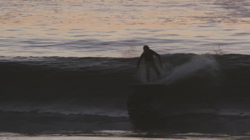 Telelphoto slowmotion shot of a Surfer riding a wave at sunset