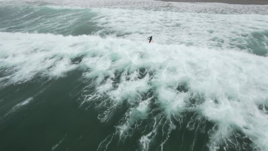 Aerial shot of a surfer riding a wave onto the shore near the coast