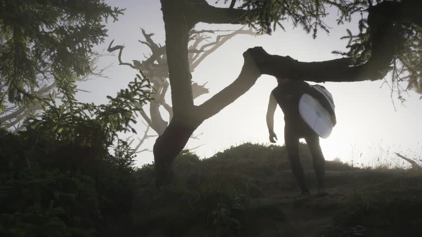 A man with a surfboard coming out of a forest