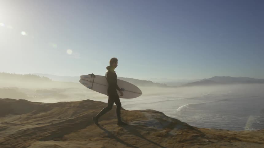 A surfer carries his surfboard on a high cliff at the shoreline