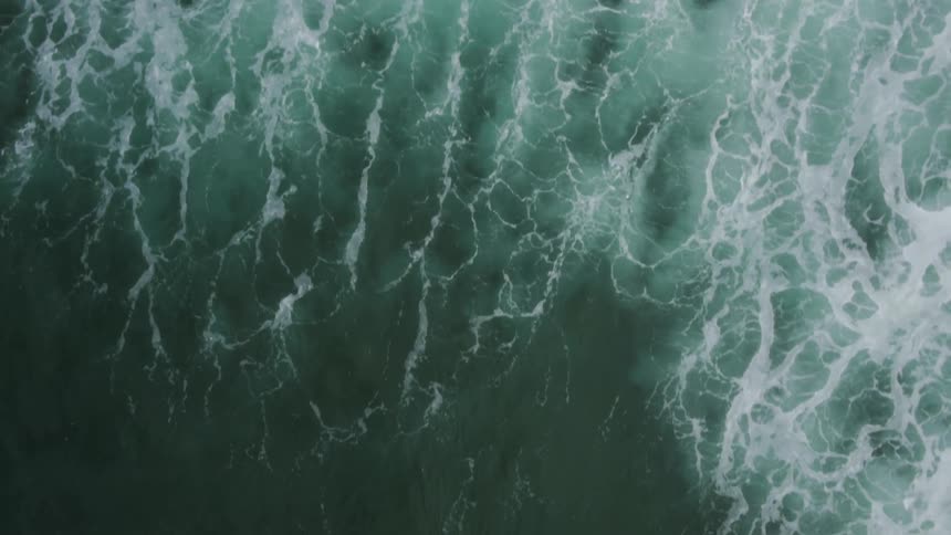 Epic Aerial reveal from sand to ocean water rushing up with the tide and then a surfer emerges from the depths of the ocean on an orange surfboard