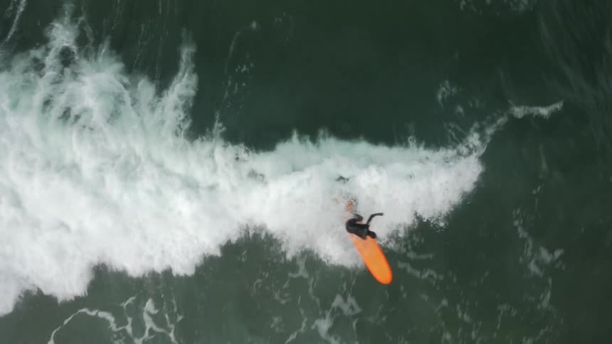 An aerial overhead view of a man surfing on an orange surfboard