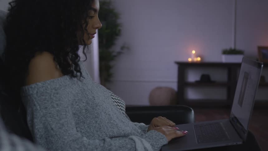 A black woman sits on a couch staring at a laptop computer